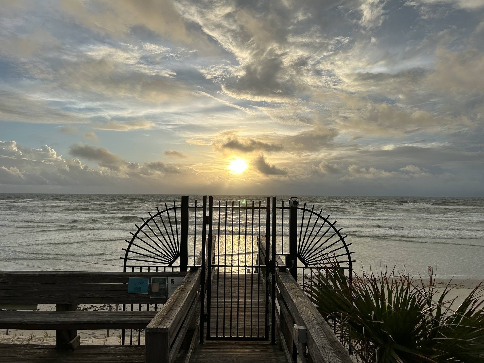 Decorative black metal beach access gate at sunset